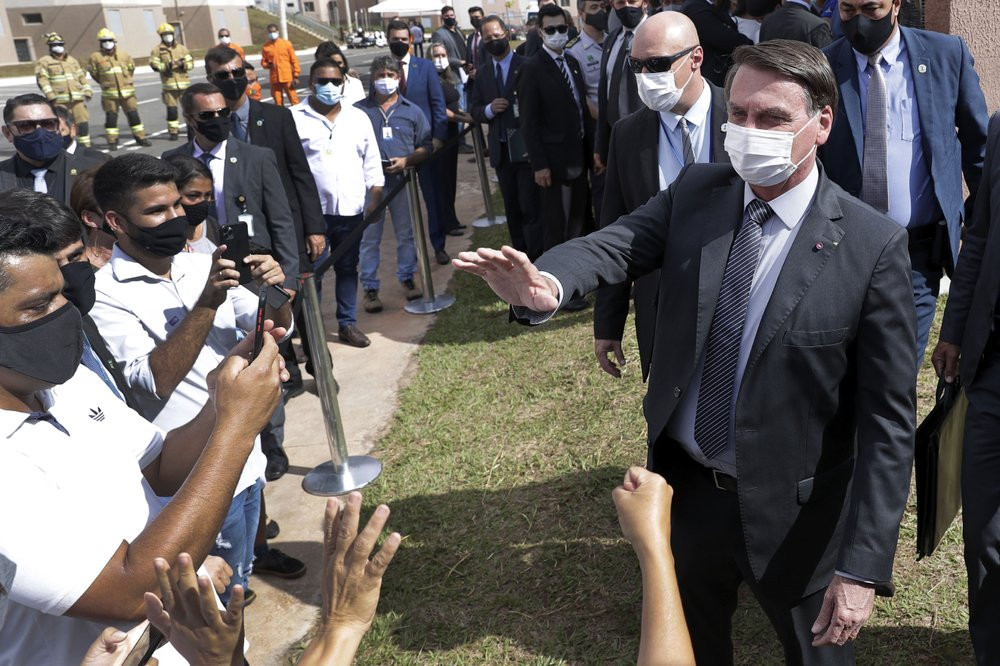 Wearing a mask to curb the spread of the new coronavirus, Brazil's President Jair Bolsonaro greets people after a ceremony to deliver affordable homes built by the government, in a neighborho