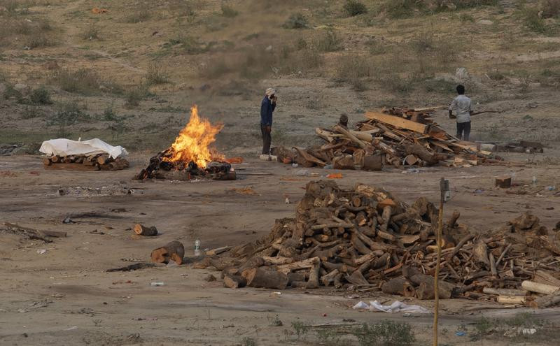Body of a COVID-19 victim lies covered in white cloth next to a burning pyre of another victim at a cremation ground in Prayagraj, India, Saturday, May 1, 2021.