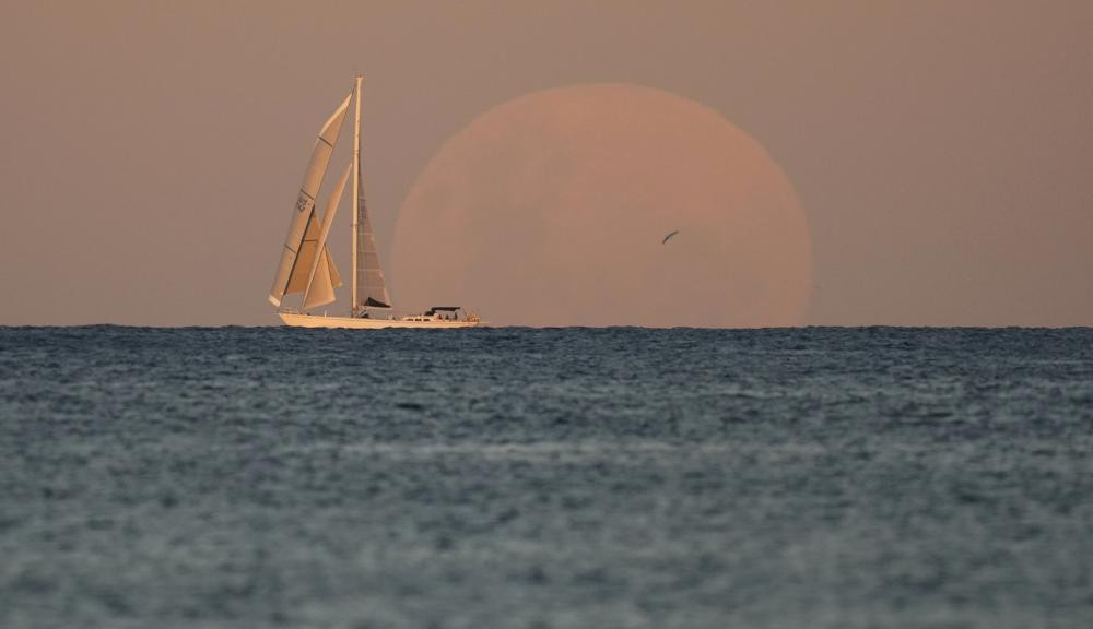 A yacht sails past as the moon rises in Sydney Wednesday, May 26, 2021.