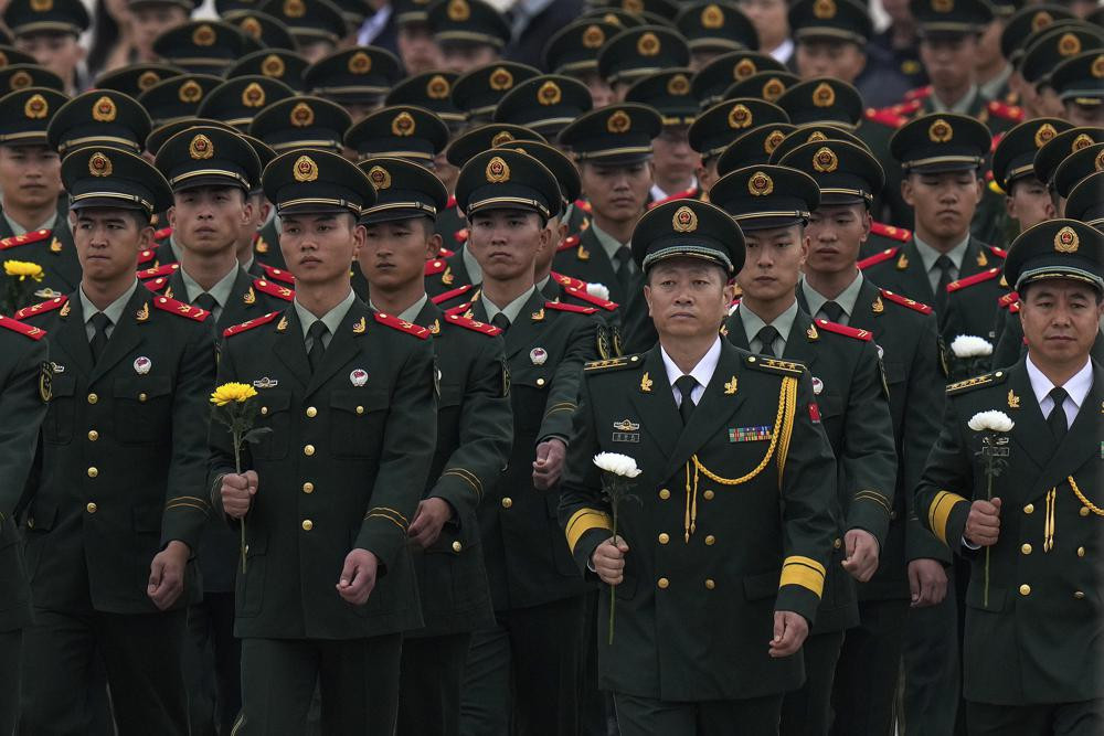 Paramilitary policemen and military officers hold flowers walk to pay respects to the People's Heroes Monument during a ceremony to mark Martyr's Day at Tiananmen Square in Beijing, Thursday,