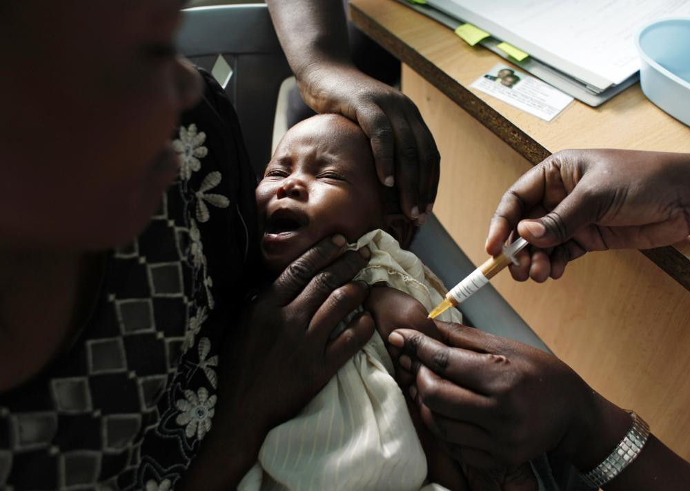 In this Oct. 30, 2009 file photo, a mother holds her baby receiving a new malaria vaccine as part of a trial at the Walter Reed Project Research Center in Kombewa in Western Kenya.