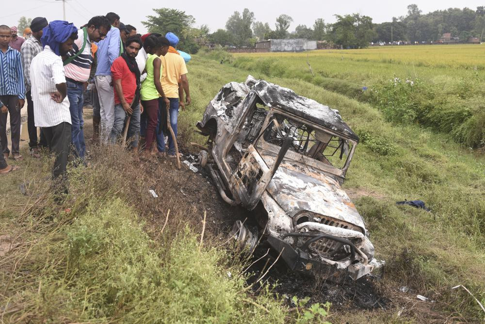 Villagers watch a burnt car which ran over and killed farmers on Sunday, at Tikonia village in Lakhimpur Kheri, Uttar Pradesh state, India, Monday, Oct. 4, 2021.