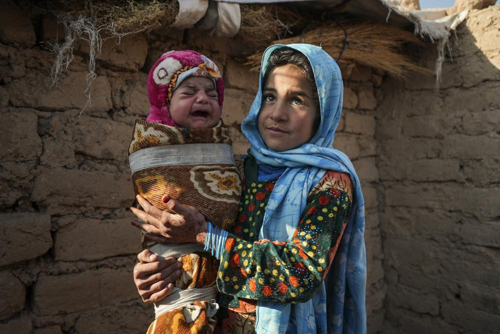 Qandi Gul holds her brother outside their home housing those displaced by war and drought near Herat. Gul’s father sold her into marriage without telling his wife, taking a down-payment so he