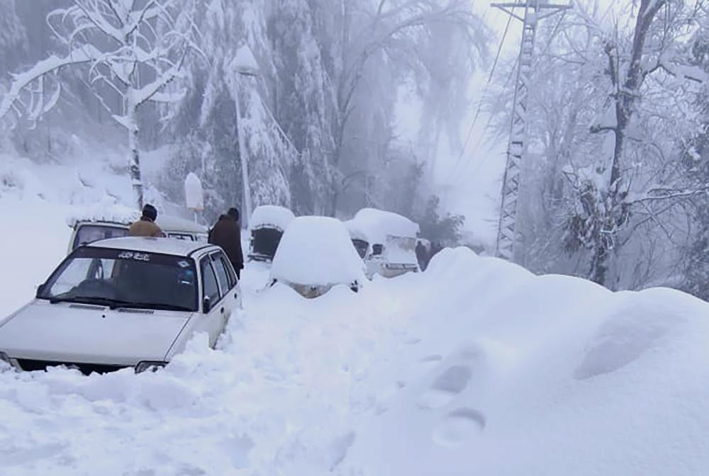 In this photo provided by the Inter Services Public Relations, people walk past vehicles trapped in a heavy snowfall-hit area in Murree, some 28 miles (45 kilometers) north of the capital of 
