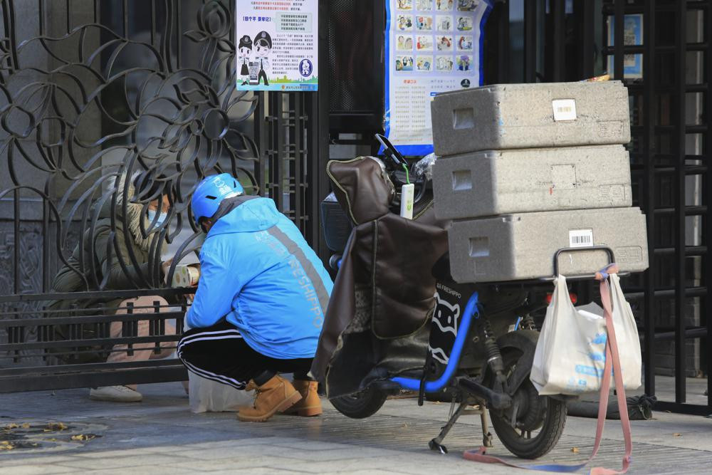 A delivery worker passes groceries to a masked woman through a closed gate at a residential block in Xi'an, a city of 13 million people under the COVID-19 lockdown, in northwest China's Shaan