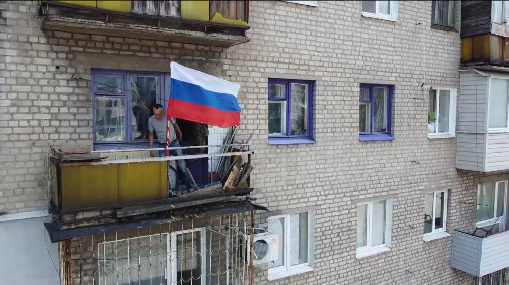 In this handout photo taken from video released by Russian Defense Ministry Press Service on Monday, July 4, 2022, a man sets a Russian national flag on a balcony of a residential building in
