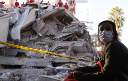 A local resident, staying outdoors for fear of aftershocks, watches as members of rescue services search for survivors in the debris of a collapsed building in Izmir, Turkey, Saturday, Oct. 3