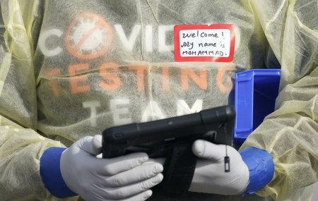 In this Oct. 28, 2020, file photo, a worker wearing gloves, and other PPE holds a tablet computer as he waits to check people at a King County coronavirus testing site in Auburn, Wash., south