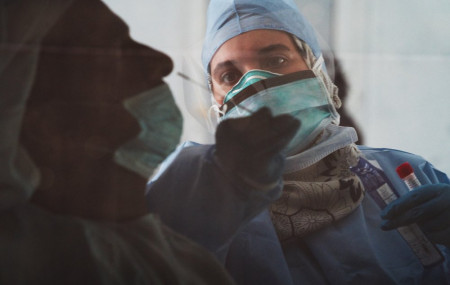 In this April 2, 2020, file photo taken through a tinted car window, a technician takes a nasal swab for a coronavirus detection test at a drive-thru testing facility in Abu Dhabi, United Ara