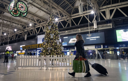 A woman pulls a suitcase past the Christmas tree on the concourse of Waterloo Station in central London, Sunday, Dec. 20, 2020.