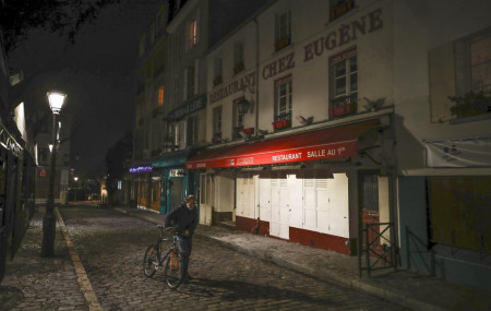 In this Dec. 15, 2020 file photo, a man pushes his bicycle along a row of closed restaurants in Montmartre, during the new imposed curfew in Paris.