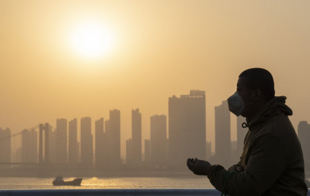 In this Jan. 15, 2021, file photo, a man wearing a mask is silhouetted as the sun sets along the riverbank in Wuhan in central China's Hubei province.