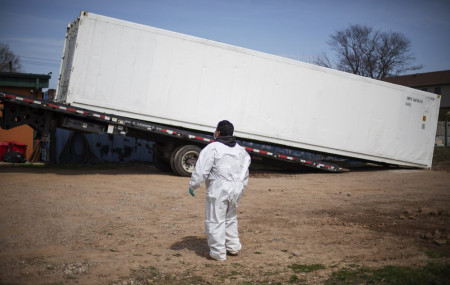 In this April 7, 2020 file photo, gravedigger Thomas Cortez watches as a refrigerated trailer is delivered to keep pace with a surge of bodies arriving for burials at the Hebrew Free Burial A