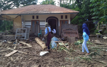 Indonesian women walk past a house damaged by flood in Waiwerang, on Adonara Island, East Nusa Tenggara province, Indonesia, Tuesday, April 6, 2021.