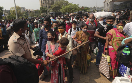 A police officer tries to control a crowd waiting to board trains at Lokmanya Tilak Terminus in Mumbai, India, Wednesday, April 14, 2021.