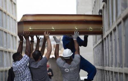 In this April 13, 2021, file photo, the remains of a woman who died from complications related to COVID-19 are placed into a niche by cemetery workers and relatives at the Inahuma cemetery in