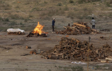 Body of a COVID-19 victim lies covered in white cloth next to a burning pyre of another victim at a cremation ground in Prayagraj, India, Saturday, May 1, 2021.