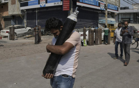 A man walks carrying a refilled cylinder as family members of COVID-19 patients wait in queue to refill their oxygen cylinders at Mayapuri area in New Delhi, India, Monday, May 3, 2021.