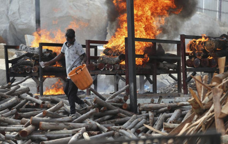 A worker sprinkles fuel on burning funeral pyres of COVID-19 victims at an open crematorium set up at a granite quarry on the outskirts of Bengaluru, India, Wednesday, May 5, 2021.