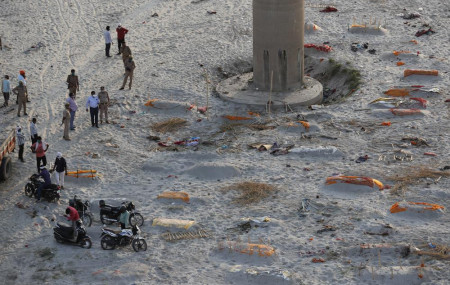 Policemen stand next to the bodies buried in shallow graves on the banks of Ganges river in Prayagraj, India, Saturday, May 15, 2021.