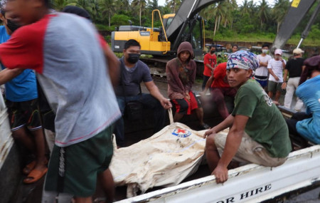 Rescuers sit beside a body bag containing the remains of a civilian victim when a Philippine military C-130 plane crashed in Patikul town, Sulu province, southern Philippines on Sunday July 4