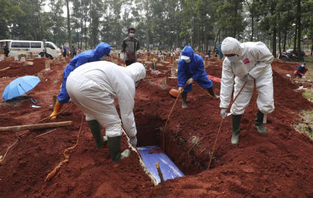 In this July 14, 2021, photo, workers in protective gear lower a coffin of a COVID-19 victim to a grave for burial at the Cipenjo Cemetery in Bogor, West Java, Indonesia.