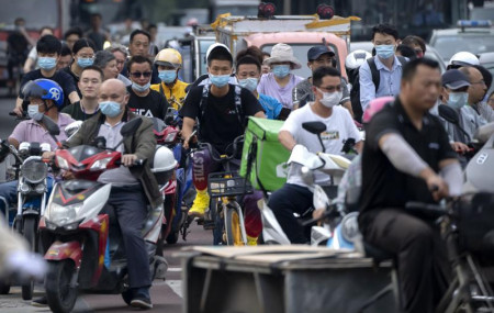 In this file photo dated Friday, July 2, 2021, people riding bicycles and scooters wait to cross an intersection during rush hour in Beijing.