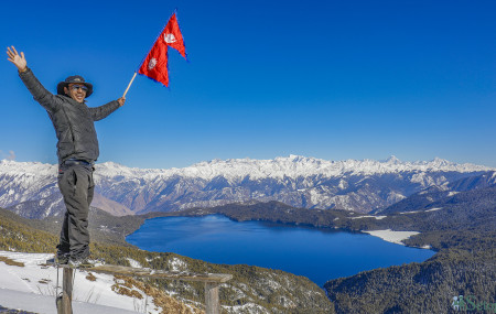 Thapa with Nepali flag at Murma Top, Mugu with Rara Lake in the background.
