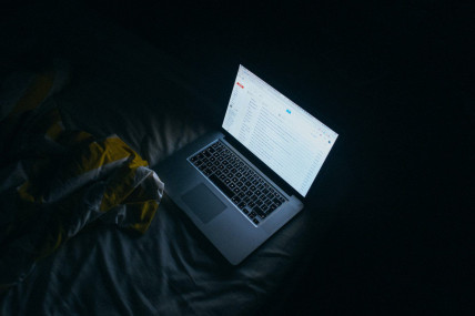 A laptop casts a glow on bedsheets at night. https://unsplash.com/photos/loAgTdeDcIU (Jay Wennington/Unsplash)