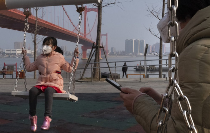 A girl wears a face mask as she play on a swing near the Yingwuzhou Yangtze River Bridge in Wuhan in central China's Hubei Province, Wednesday, Jan. 29, 2020.