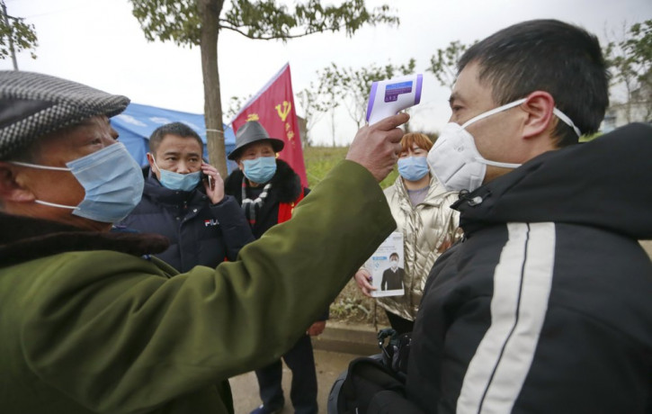 In this Saturday, Feb. 1, 2020, photo, a government worker takes the temperature of a passer-by at a checkpoint in Suining in southwestern China's Sichuan Province.