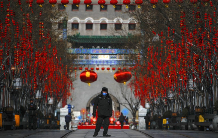 A security guard wearing a face mask walks through a quiet main Qianmen Street, a popular tourist spot, in Beijing, Sunday, Feb. 16, 2020.