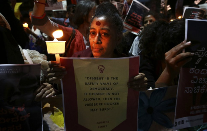 In this Tuesday, Feb. 4, 2020 photo, an Indian woman holds a candle and placard during a protest against the sedition case filed by police against a school after a play preformed by students 