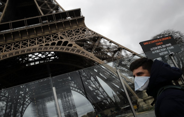A man wearing a mask walks pasts the Eiffel tower closed after the French government banned all gatherings of over 100 people to limit the spread of the virus COVID-19, in Paris, Saturday, Ma