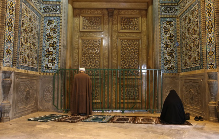 A cleric and a woman pray behind a closed door of Masoume shrine in the city of Qom, some 80 miles (125 kilometers) south of the capital Tehran, Iran, Monday, March 16, 2020.