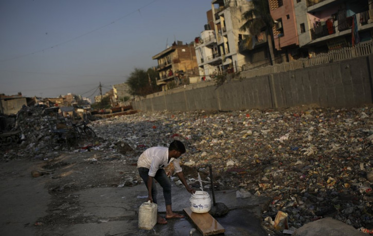 In this Tuesday, March 17, 2020 photo, a slum dweller fills water from a tap next to a drain filled with plastic and other filth in New Delhi, India.
