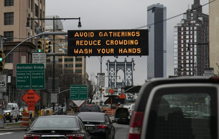 In this March 19, 2020, file photo, the Manhattan bridge is seen in the background of a flashing sign urging commuters to avoid gatherings, reduce crowding and to wash hands in the Brooklyn b