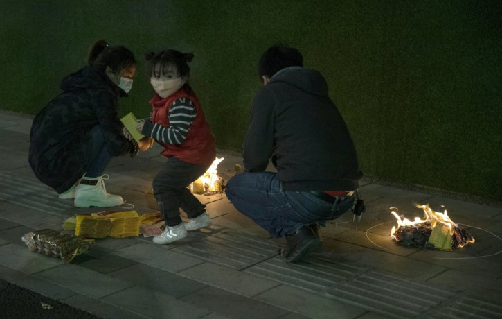 A family burn paper offerings for their departed relatives on the streets of Wuhan in central China's Hubei province on Saturday, April 4, 2020.