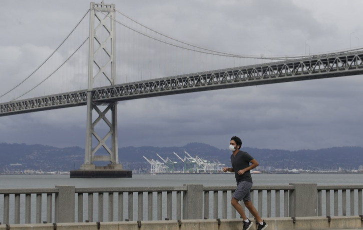 A man wears a mask to protect himself from the coronavirus while running in front of the San Francisco-Oakland Bay Bridge along the Embarcadero in San Francisco, Sunday, April 5, 2020.