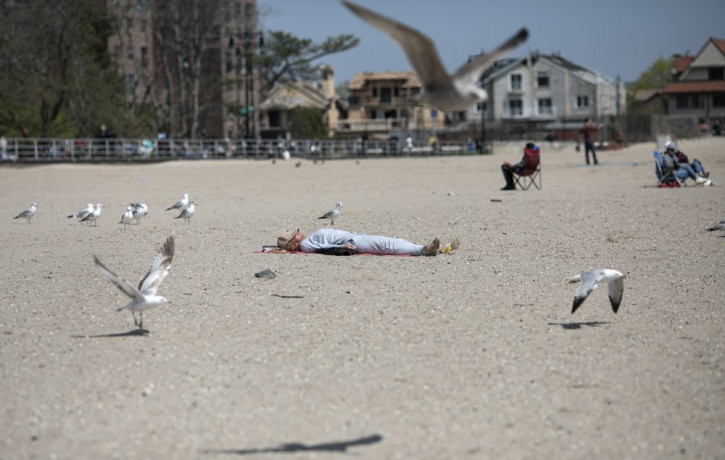 A woman sleeps on Brighton Beach in the Brooklyn borough of New York as seagulls flutter around her, on Saturday, April 25, 2020.