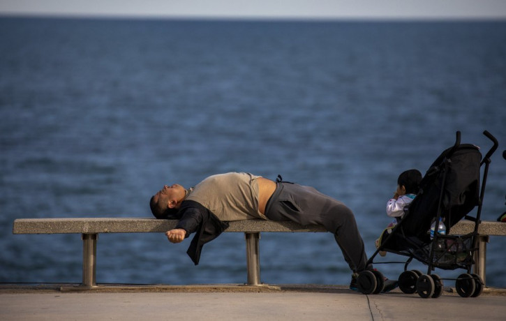A man lies on a bench in front of the Mediterranean sea in Barcelona, Spain, Sunday, April 26, 2020 as the lockdown to combat the spread of coronavirus continues.