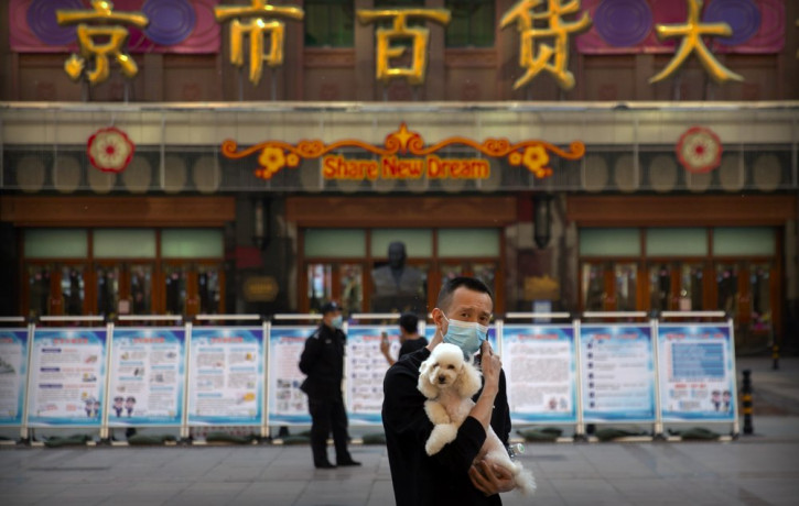 A man wearing a face mask to prevent the spread of the new coronavirus holds a dog as he stands along a pedestrian shopping street in Beijing, Tuesday, April 28, 2020.