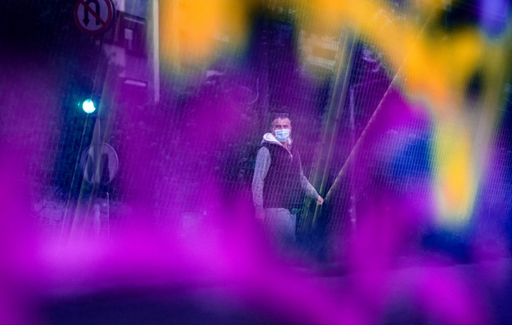 Seen through a bridge glass panel covered in graffiti a man wearing a face mask walks in Sarajevo, Bosnia, Wednesday, May 6, 2020.