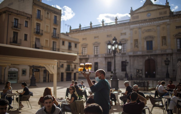 A waiter carries beers for customers sitting on a terrace bar in Tarragona, Spain, Monday, May 11, 2020.