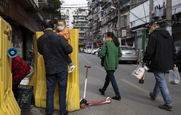In this photo taken Wednesday, April 1, 2020, residents walk past a sealed off neighborhood in Wuhan, central China's Hubei province.