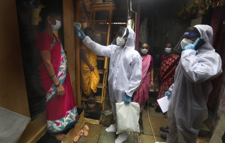 A health worker checks the body temperature of a resident, as others await their turn during a free medical checkup in a slum in Mumbai, India, Sunday, June 28, 2020.
