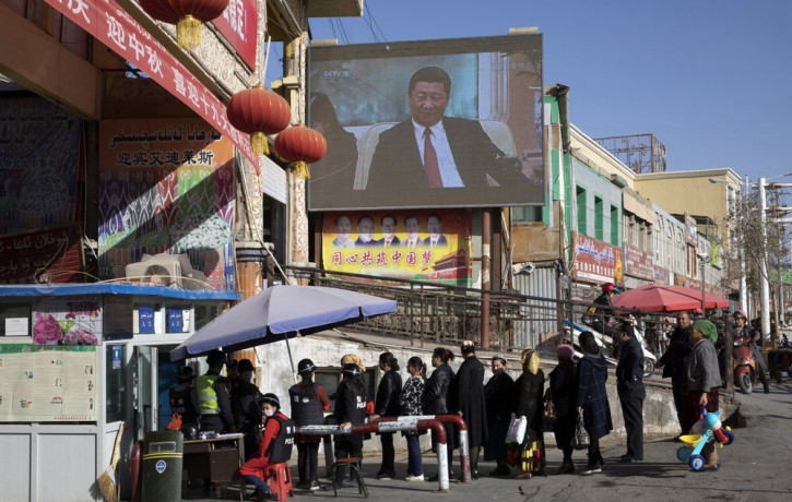 In this Nov. 3, 2017, file photo, residents line up at a security checkpoint into the Hotan Bazaar where a screen shows Chinese President Xi Jinping in Hotan in western China's Xinjiang regio