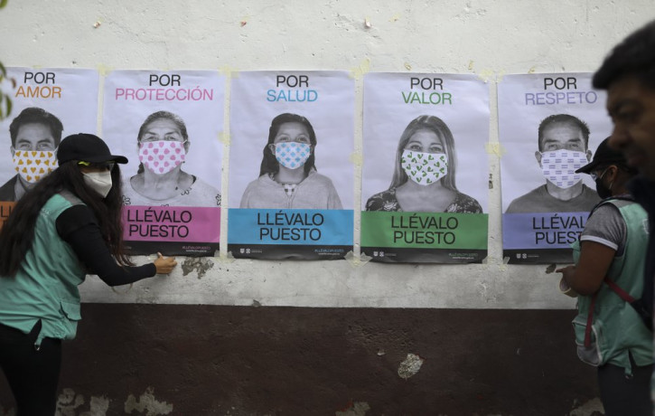 A man not wearing a face mask walks by as city health department workers affix a series of posters advocating mask use to a wall, in San Mateo Xalpa in the Xochimilco district of Mexico City,