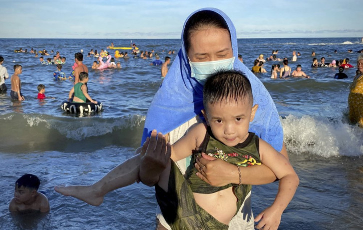 A woman wearing a mask carries her child on a beach in Vung Tau city, Vietnam, Sunday, July 26, 2020.
