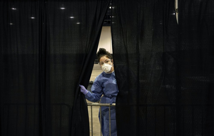 Diana Vega, a registered respiratory therapist, peeks through a curtain during setup at a temporary coronavirus testing site Monday, Aug. 3, 2020, in Las Vegas.